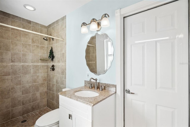 bathroom featuring a tile shower, vanity, and toilet