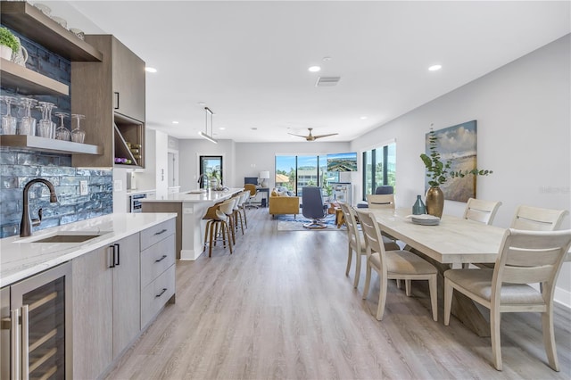 dining area with sink, ceiling fan, light hardwood / wood-style floors, and beverage cooler