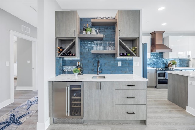 kitchen with wall chimney range hood, beverage cooler, stainless steel stove, light wood-type flooring, and sink