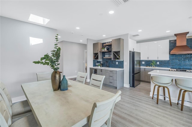 dining room featuring sink, light hardwood / wood-style flooring, and a skylight