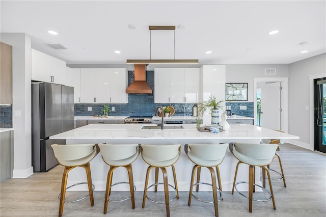 kitchen featuring white cabinets, hanging light fixtures, stainless steel refrigerator, custom range hood, and sink