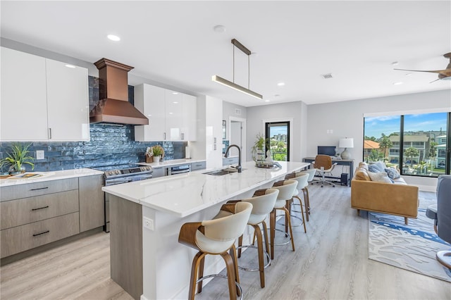 kitchen with an island with sink, hanging light fixtures, sink, white cabinets, and light hardwood / wood-style floors