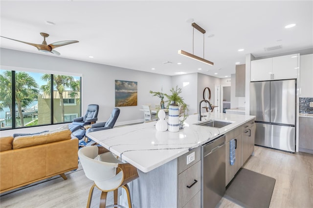 kitchen with white cabinetry, stainless steel appliances, decorative light fixtures, and an island with sink