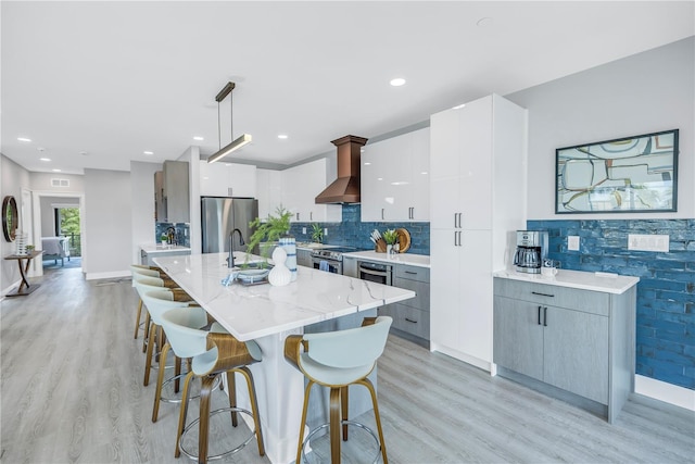 kitchen with a kitchen island with sink, stainless steel appliances, pendant lighting, light wood-type flooring, and white cabinets