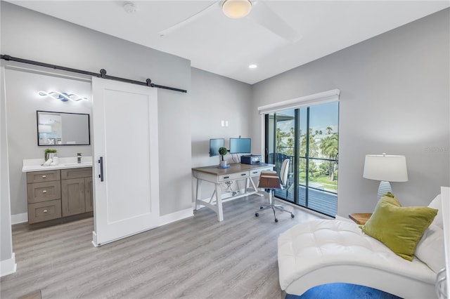 office featuring light hardwood / wood-style flooring, a barn door, and ceiling fan