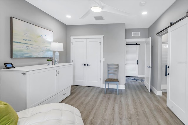 bedroom featuring a closet, ceiling fan, light hardwood / wood-style floors, and a barn door