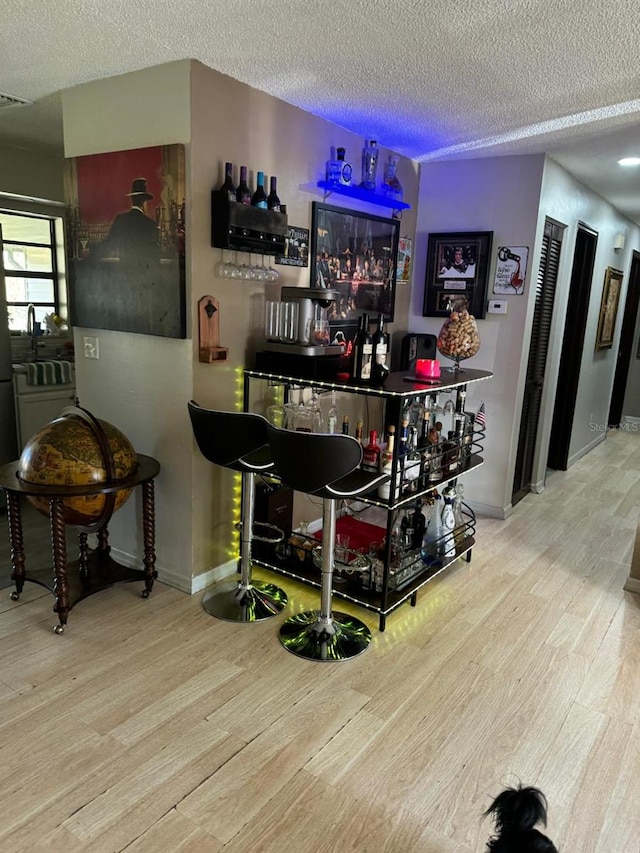 bar with a textured ceiling, light wood-type flooring, and fridge