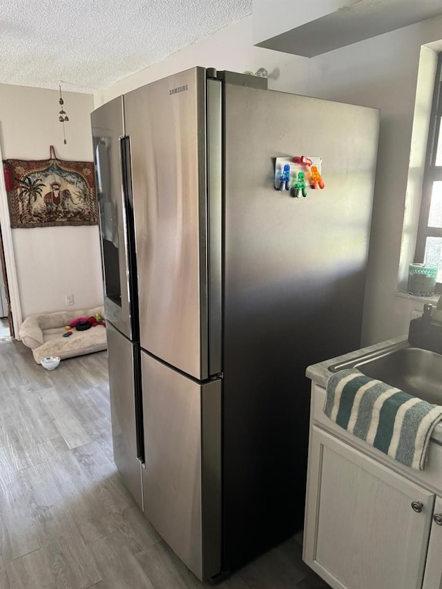 111 Carillo St NE, Palm Bay, FL 32907 - kitchen with stainless steel fridge, wood finished floors, a textured ceiling, a sink, and white cabinetry