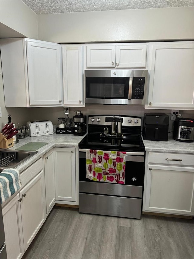 kitchen with appliances with stainless steel finishes, light hardwood / wood-style flooring, a textured ceiling, and white cabinets