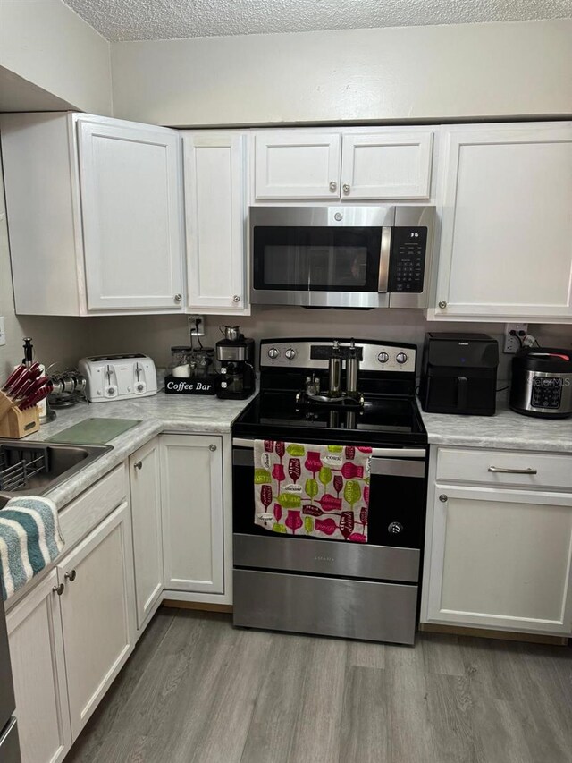 111 Carillo St NE, Palm Bay, FL 32907 - kitchen featuring stainless steel appliances, light wood finished floors, white cabinetry, light countertops, and a textured ceiling