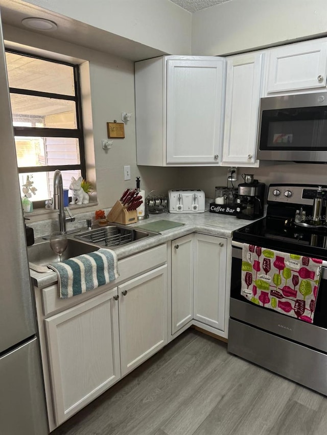 kitchen with light hardwood / wood-style floors, white cabinets, stainless steel appliances, and sink