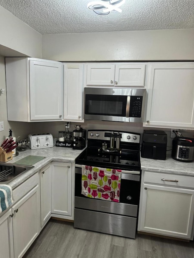 kitchen with white cabinetry, stainless steel appliances, a textured ceiling, and light hardwood / wood-style flooring