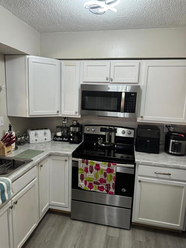 111 Carillo St NE, Palm Bay, FL 32907 - kitchen featuring appliances with stainless steel finishes, a textured ceiling, white cabinets, light wood-style floors, and light countertops