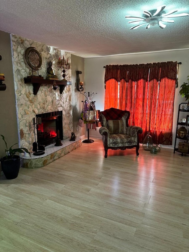 living room featuring a stone fireplace, a textured ceiling, wood-type flooring, and ceiling fan