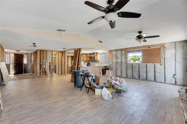 living room featuring lofted ceiling, light hardwood / wood-style flooring, a textured ceiling, and ceiling fan