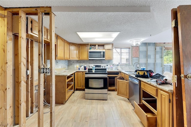 kitchen featuring light stone countertops, sink, a textured ceiling, stainless steel appliances, and light hardwood / wood-style flooring