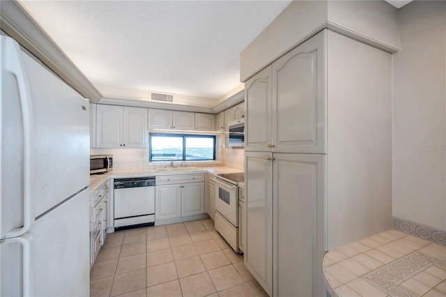 kitchen with light tile patterned floors, white cabinets, a textured ceiling, white appliances, and tasteful backsplash