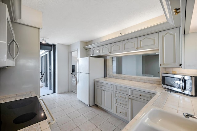 kitchen featuring white appliances, a textured ceiling, and tile counters