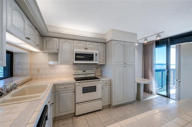 kitchen with rail lighting, light tile patterned floors, tile counters, sink, and white appliances