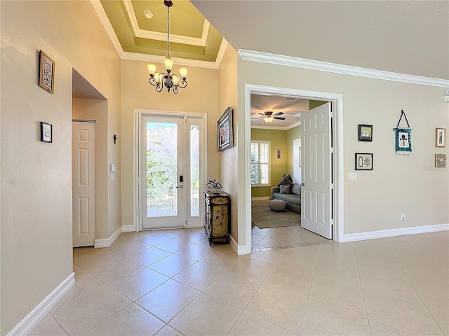 entryway with ornamental molding, a raised ceiling, ceiling fan with notable chandelier, and light tile patterned floors