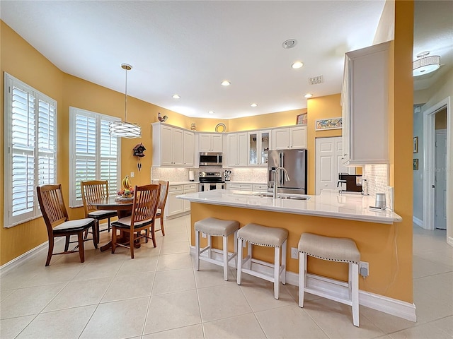 kitchen with white cabinets, hanging light fixtures, appliances with stainless steel finishes, a kitchen bar, and sink