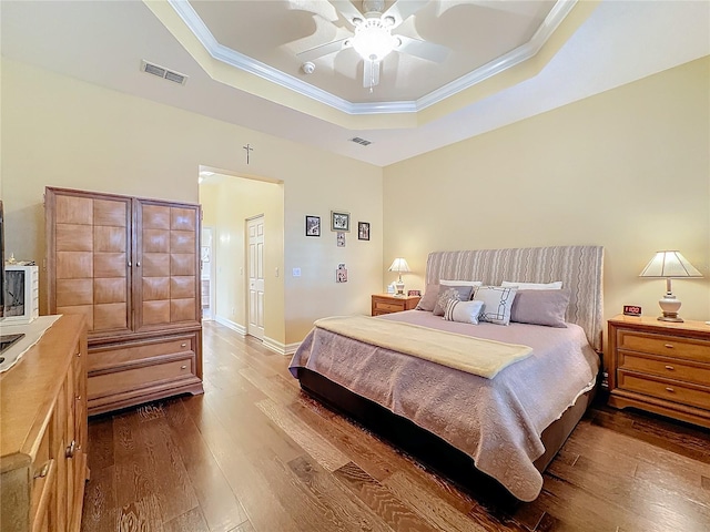 bedroom with ornamental molding, hardwood / wood-style flooring, a raised ceiling, and ceiling fan