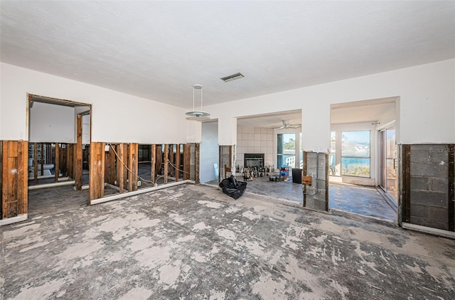 unfurnished living room with ceiling fan and a tiled fireplace