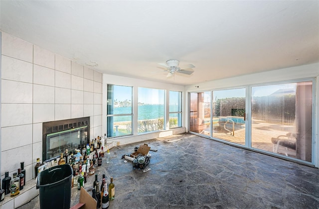 unfurnished living room with ceiling fan, a fireplace, a water view, and tile walls