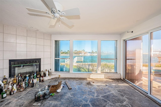 sunroom / solarium featuring a water view, ceiling fan, and a tiled fireplace