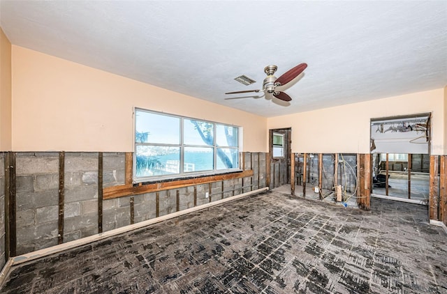 interior space featuring ceiling fan, a textured ceiling, and tile walls