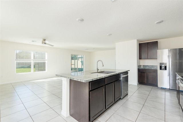 kitchen featuring a kitchen island with sink, dark brown cabinets, stainless steel appliances, sink, and light tile patterned floors