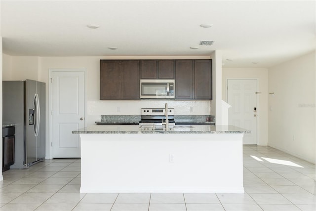 kitchen featuring light stone countertops, appliances with stainless steel finishes, dark brown cabinetry, light tile patterned floors, and a center island with sink