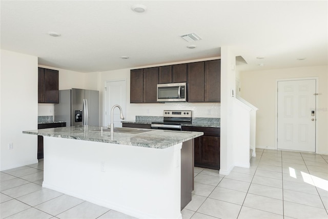 kitchen with stainless steel appliances, dark brown cabinetry, light tile patterned floors, and an island with sink