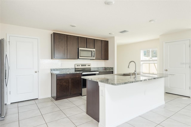 kitchen with a center island with sink, sink, light stone countertops, light tile patterned flooring, and appliances with stainless steel finishes