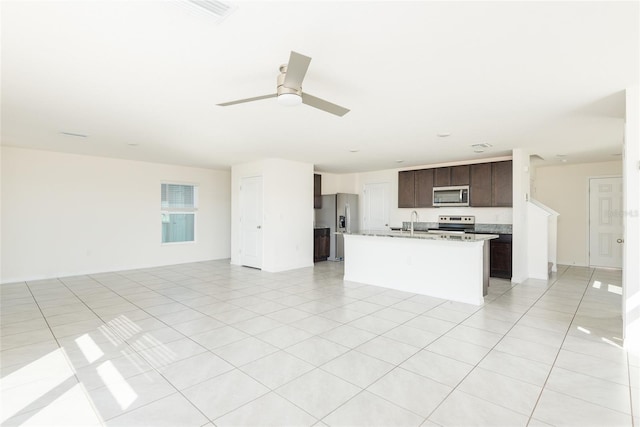 kitchen featuring appliances with stainless steel finishes, sink, dark brown cabinets, light tile patterned floors, and a kitchen island with sink