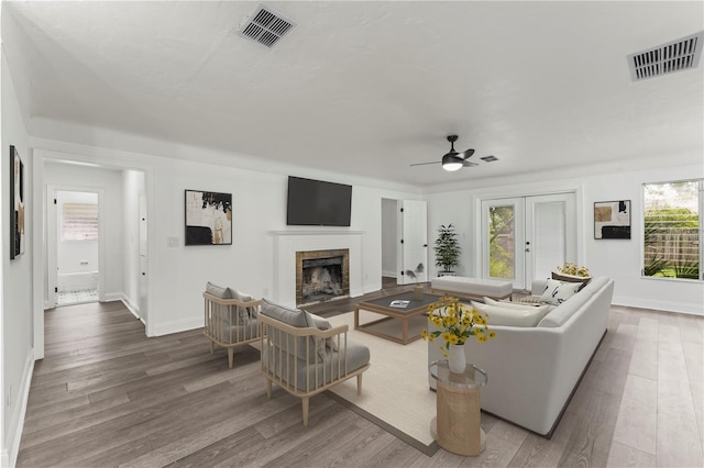 living room with french doors, a tiled fireplace, light wood-type flooring, and ceiling fan