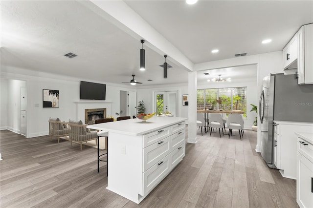 kitchen featuring light wood-type flooring, ceiling fan with notable chandelier, a center island, a kitchen breakfast bar, and white cabinetry