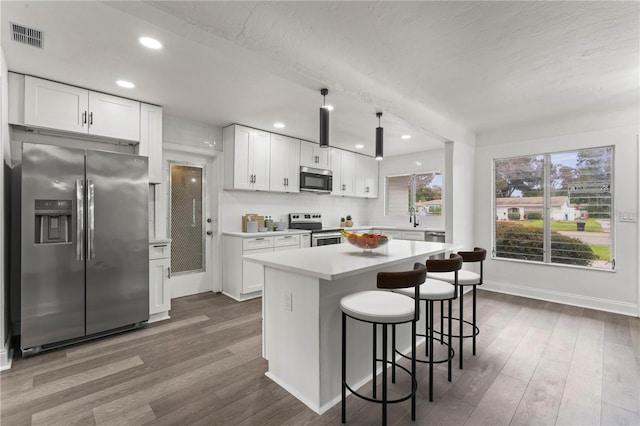 kitchen featuring hardwood / wood-style floors, white cabinetry, a kitchen breakfast bar, and stainless steel appliances