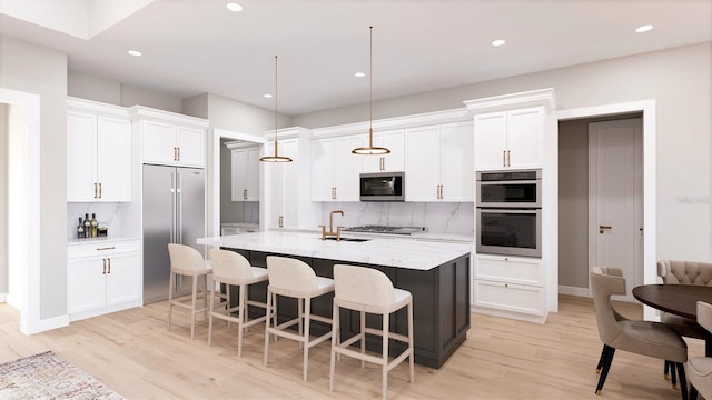 kitchen with appliances with stainless steel finishes, an island with sink, hanging light fixtures, white cabinets, and light stone counters