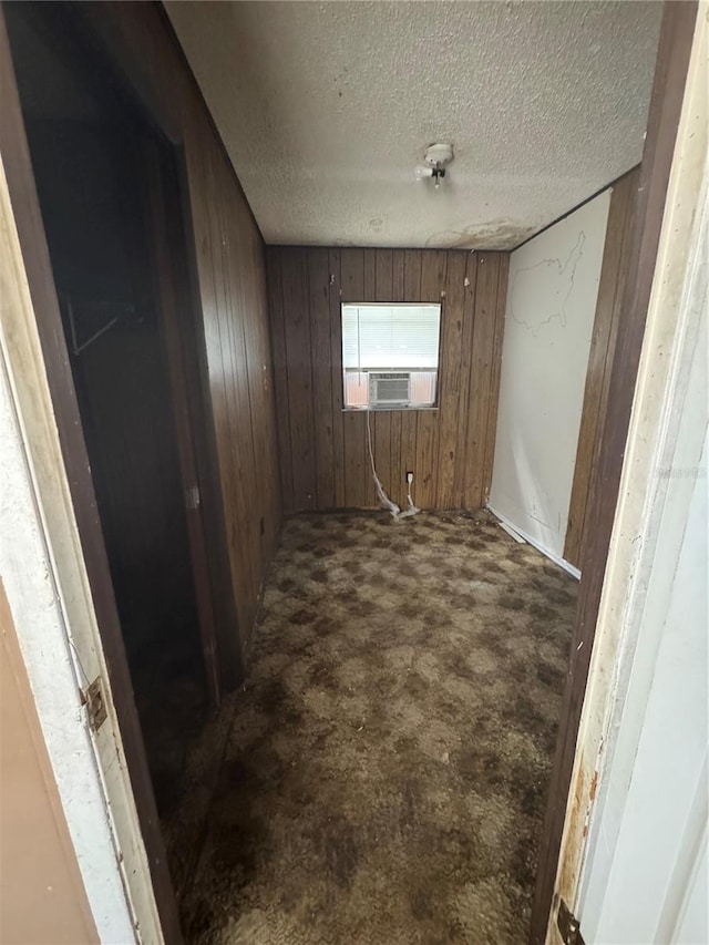 unfurnished room featuring cooling unit, a textured ceiling, wood walls, and dark colored carpet