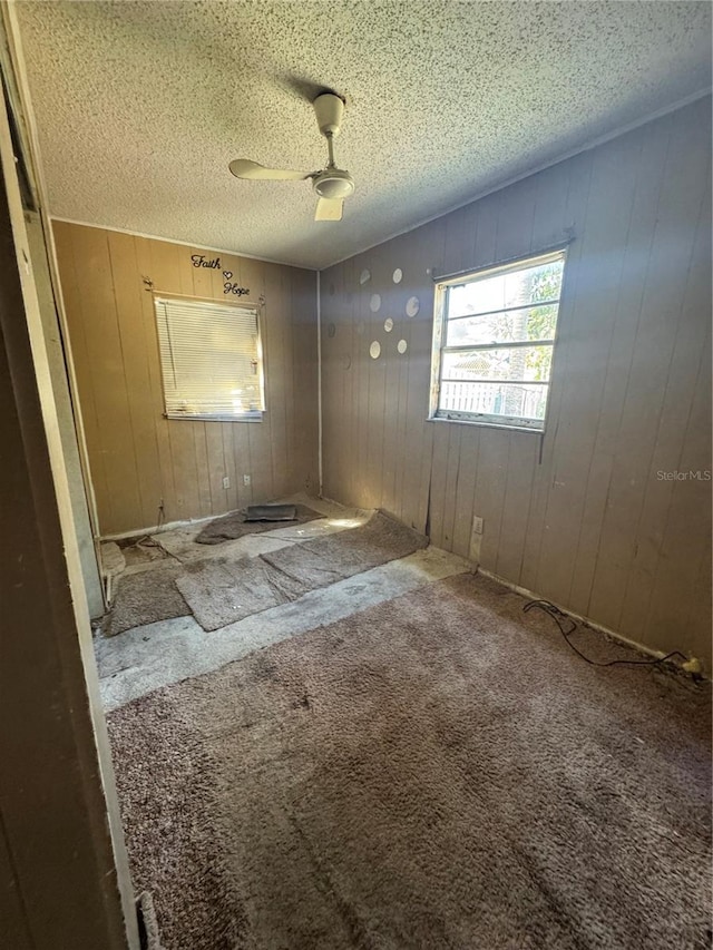 empty room with ceiling fan, wood walls, carpet flooring, and a textured ceiling