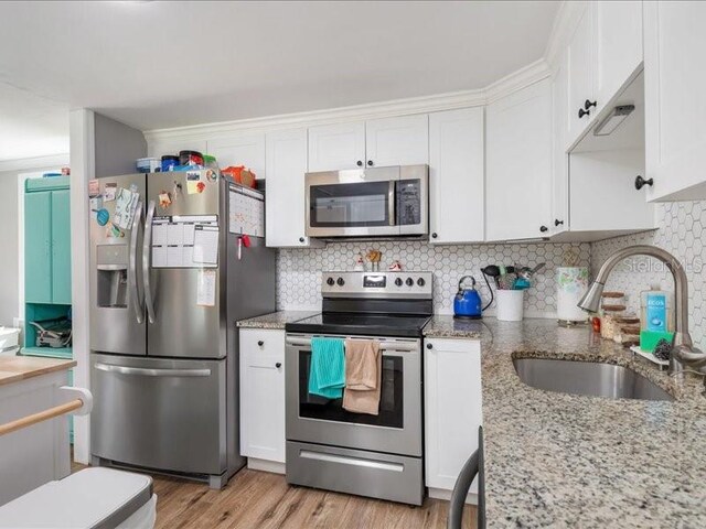 kitchen with appliances with stainless steel finishes, sink, light hardwood / wood-style floors, white cabinets, and light stone counters