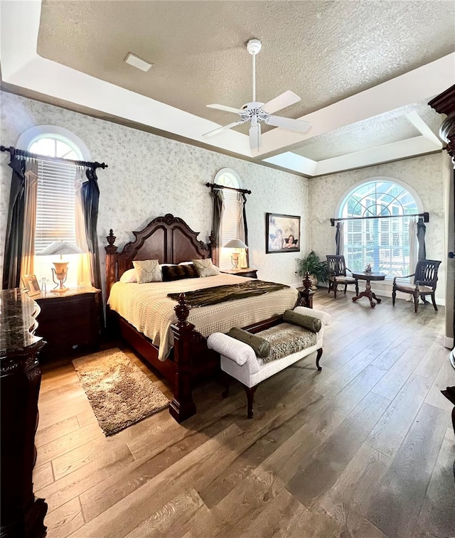 bedroom with hardwood / wood-style floors, ceiling fan, and a raised ceiling