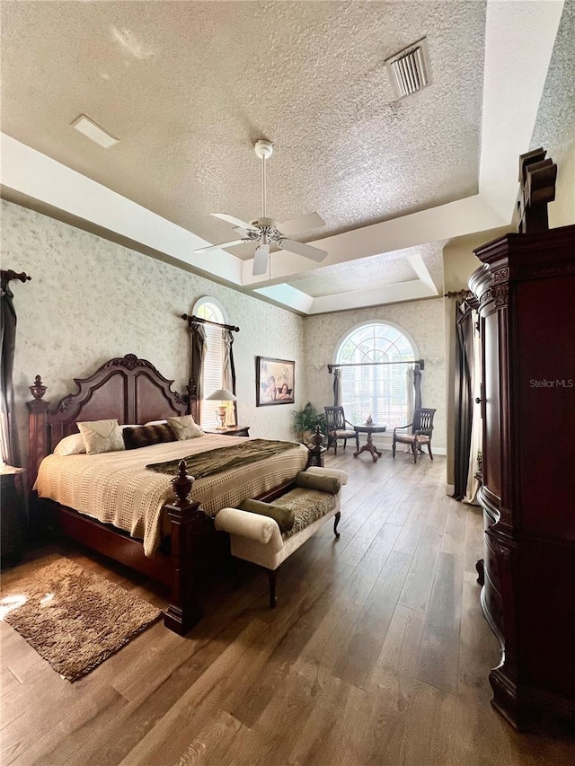 bedroom featuring hardwood / wood-style floors, ceiling fan, a textured ceiling, and a tray ceiling