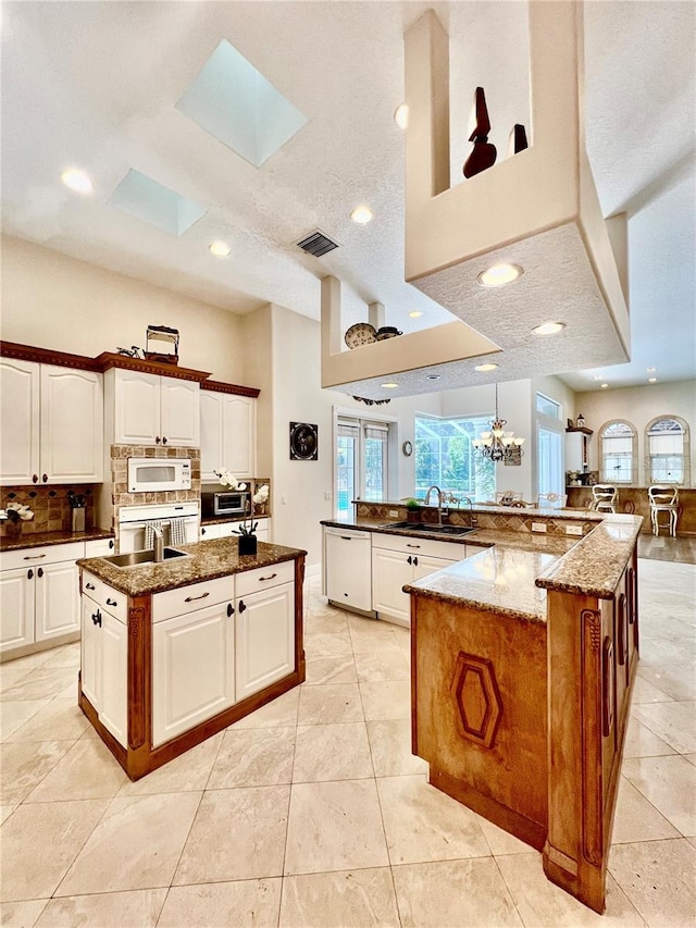 kitchen with white appliances, a skylight, a spacious island, and dark stone countertops