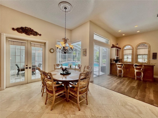 tiled dining room featuring a notable chandelier, a healthy amount of sunlight, a textured ceiling, and french doors