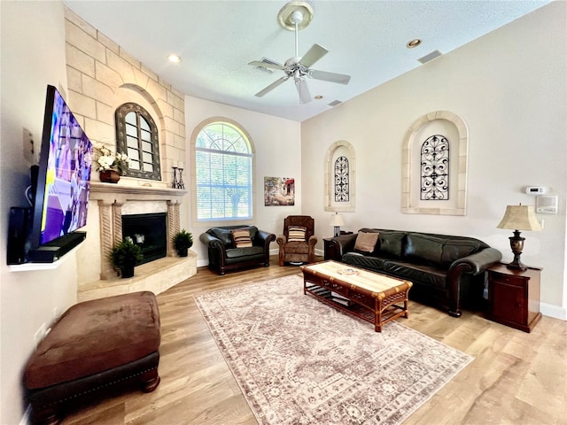 living room with a textured ceiling, a large fireplace, light hardwood / wood-style flooring, and ceiling fan