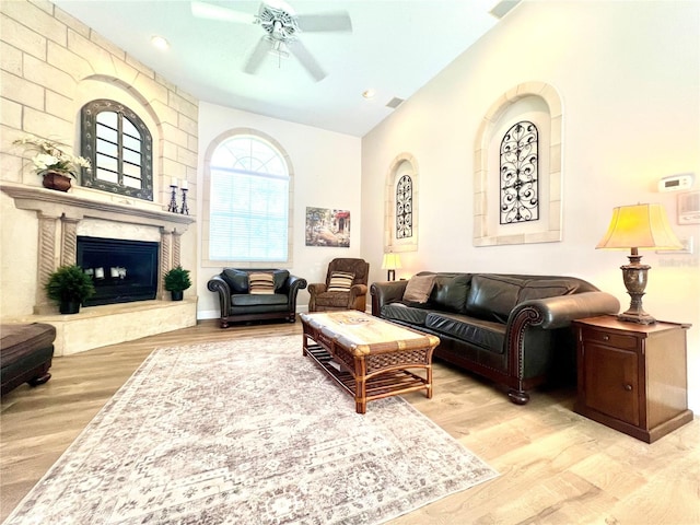 living room featuring light wood-type flooring, vaulted ceiling, ceiling fan, and a premium fireplace