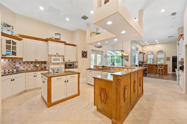 168 Rue Des Chateaux, Tarpon Springs, FL 34688 - kitchen featuring a spacious island, white appliances, tasteful backsplash, glass insert cabinets, and dark stone counters