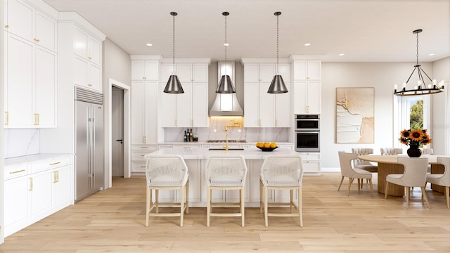 kitchen with wall chimney range hood, white cabinets, a center island with sink, and pendant lighting